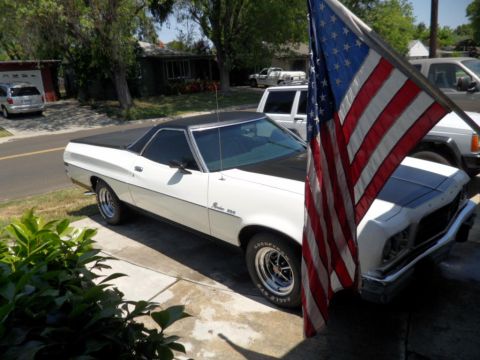 1973 Ford Ranchero - A white Ford Ranchero with a black top and hood is parked in a driveway, partially obscured by an American flag.