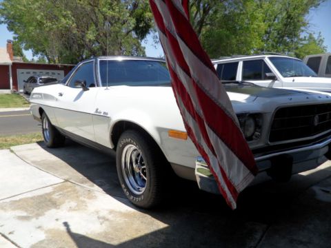 1973 Ford Ranchero - A white 1973 Ford Ranchero is parked in a driveway next to another vehicle, partially hidden by an American flag.