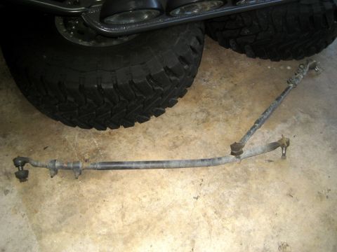 1996 Ford Bronco - Steering linkage assembly, likely for an off-road vehicle, shown with large tires in the background.