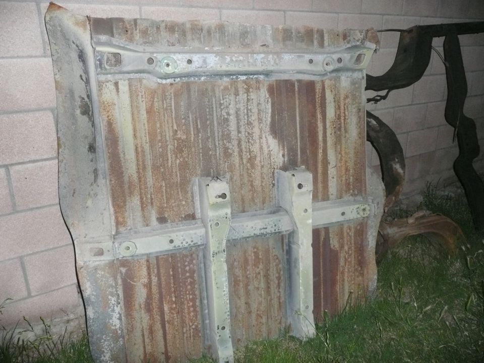 Rusted metal panel with two vertical mounting brackets, leaning against a brick wall