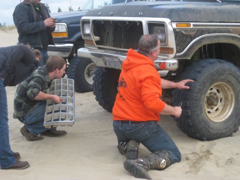 1979 Ford Bronco - People inspect a lifted Ford truck on a sandy terrain, with another vehicle visible in the background.