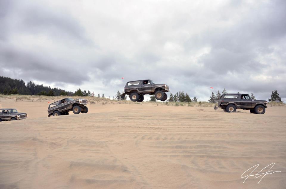 Four dark Ford Broncos driving on sand dunes under a cloudy sky