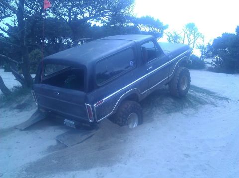 1979 Ford Bronco - Ford Bronco stuck in sand with rear wheels on ramps, trees and a flag in background.