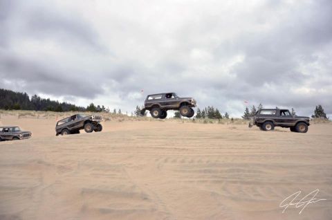 1979 Ford Bronco - Multiple SUVs are captured mid-air and on the ground as they traverse sandy terrain.