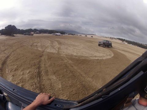 1979 Ford Bronco - A dark 1979 Ford Bronco navigates sandy terrain under a cloudy sky, with other vehicles visible in the distance.