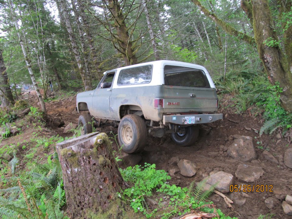 GMC K5 Blazer driving on a dirt trail in the woods, going over rocks