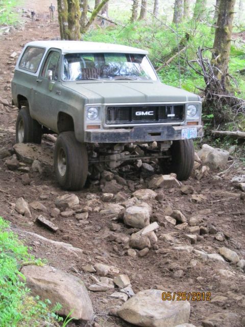 1979 Ford Bronco - A lifted GMC K5 Blazer navigates a rocky off-road trail in a wooded area.