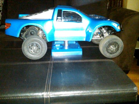 1986 Ford Bronco - RC truck body displayed on a stand, revealing its suspension and wheel assembly.
