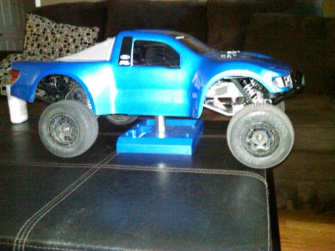 1986 Ford Bronco - A blue remote control truck body is displayed on a stand, revealing its suspension and wheels.