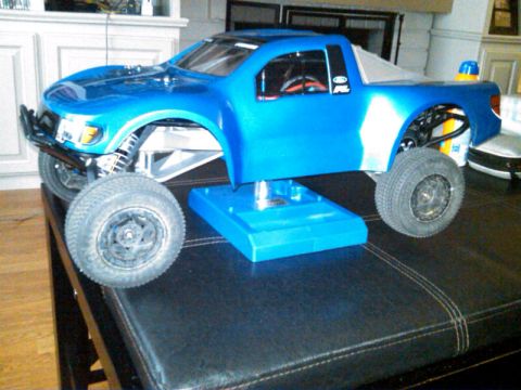 1986 Ford Bronco - This blue remote control truck is displayed on a blue stand on a dark surface.
