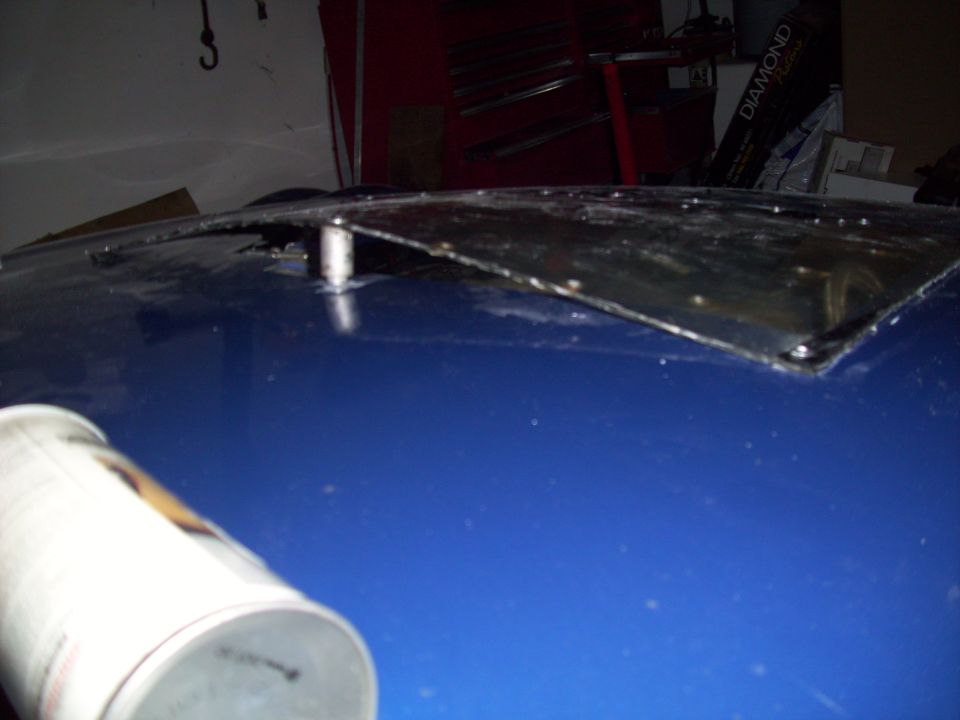 Blue car hood with a detached, bent metal panel held by a single bolt