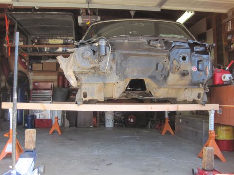 1989 Ford Bronco - The front end of a vehicle is disassembled and supported by jack stands in a garage.
