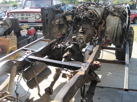1989 Ford Bronco - A red 1989 Ford Bronco is parked behind a disassembled black Bronco chassis, showing the engine and drivetrain components.