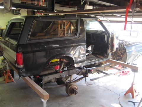 1989 Ford Bronco - The body of a black SUV is elevated above its chassis, indicating a significant repair or modification process.