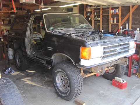 1989 Ford Bronco - This black Ford Bronco is undergoing repairs in a garage, with its doors removed and hood open.