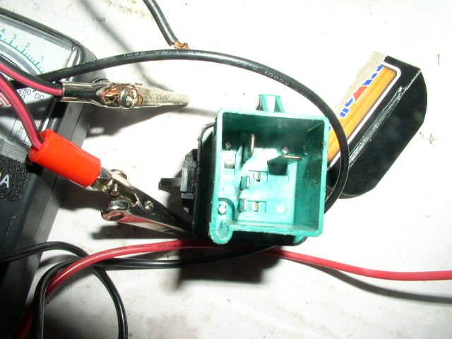 Multimeter testing a green automotive relay with alligator clip leads