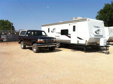 1994 Ford Bronco - A dark-colored Ford Bronco is parked beside a white travel trailer under a clear blue sky.