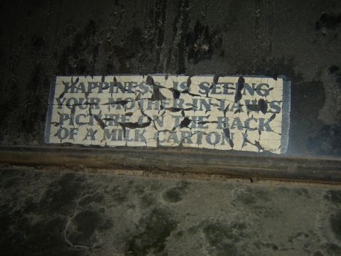 1984 Ford Mustang - A weathered sign displays a humorous quote about happiness and a mother-in-law's picture on a milk carton.
