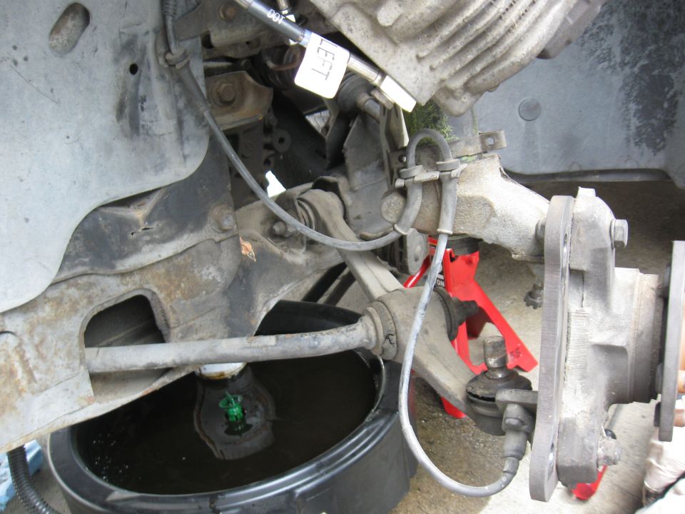 car's front suspension with a red jack stand and a drain pan collecting fluid