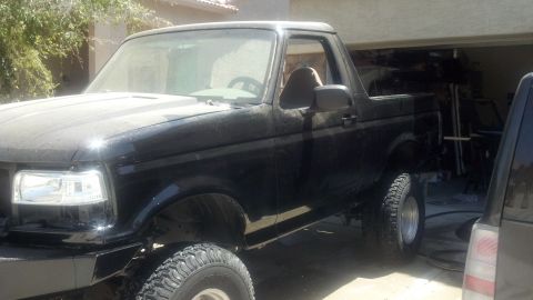 1995 Ford Bronco - A black Ford Bronco is shown from a three-quarter front angle, parked inside a garage with another vehicle partially visible.