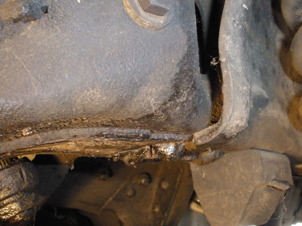 Close-up of a greasy, corroded vehicle frame section with visible suspension parts and a SuperMotors.net watermark
