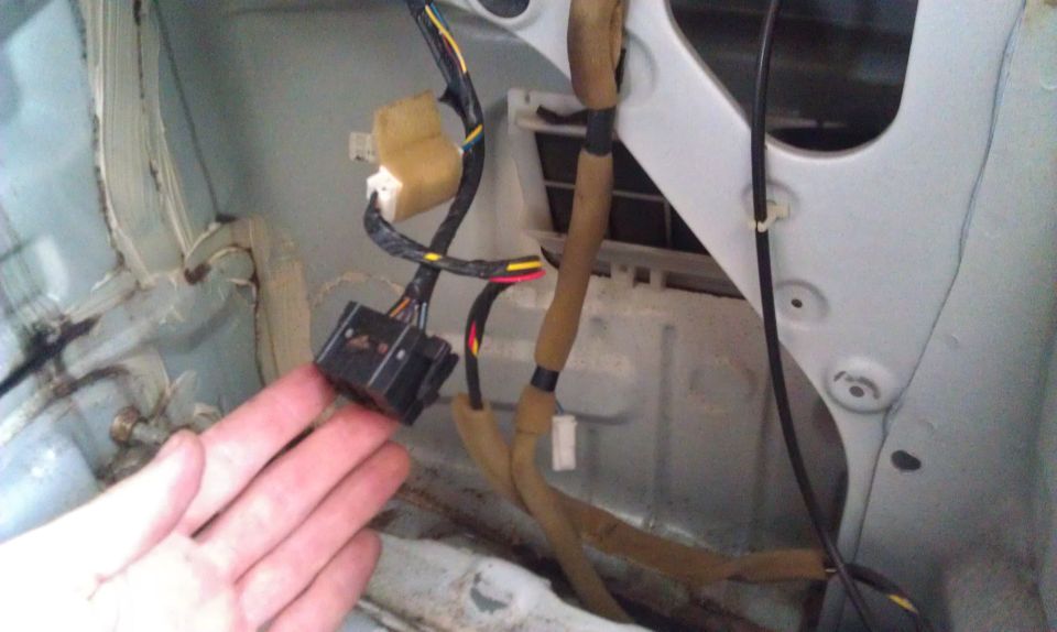 Hand holding black electrical connector near wiring harness inside a vehicle's interior