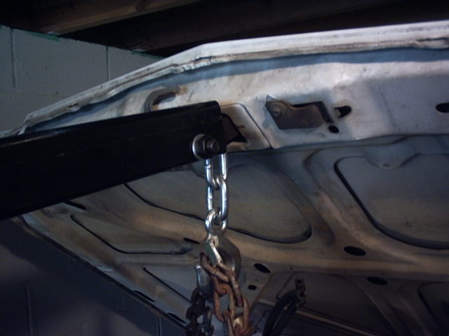 Underside of a white body panel lifted by a chain and shackle from a black hoist arm