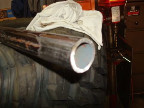 1995 Ford Bronco - A metal pipe lies on a tire next to a drill press in a workshop setting.