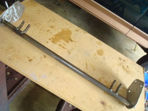 1995 Ford Bronco - A metal rod with mounting plates and prongs is shown on a wooden surface, possibly a vehicle part.