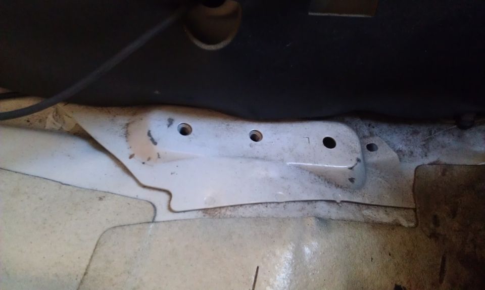 Close-up of a car's interior floor pan with some rust and mounting holes visible