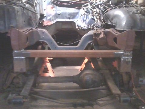 1985 Ford Bronco - The front suspension and frame of a vehicle are supported by jack stands in a workshop setting.