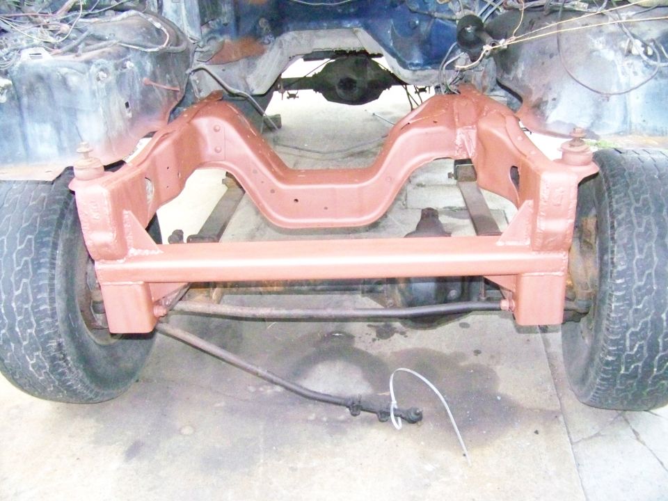 Vehicle frame with red-painted suspension components and front wheels. Some wiring is visible