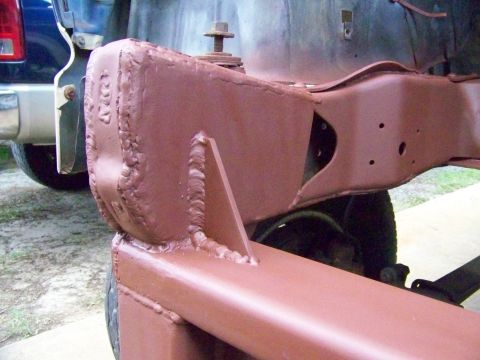 1985 Ford Bronco - Close-up of heavily welded vehicle frame components, with a blue truck in the background.