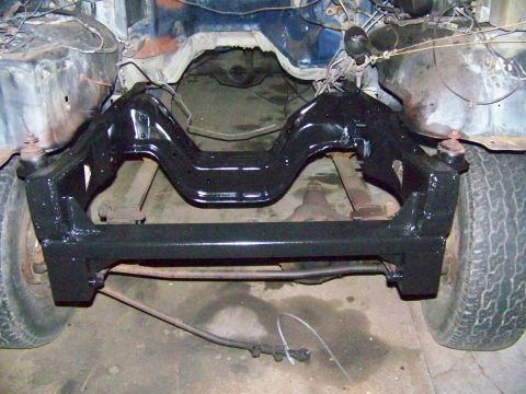 1985 Ford Bronco - The front suspension and frame of a vehicle are visible, with black paint applied to the suspension components.