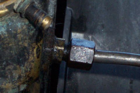 1980 Ford Bronco - Extreme close-up of a hard steel line threaded into a brass fitting with a hex tube nut passing through a bracket, next to a corroded brass…