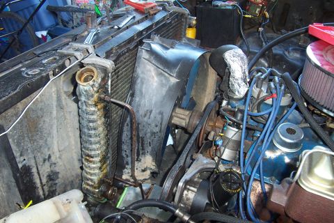 1980 Ford Bronco - Engine bay of a Ford V8 with the grille and core support opened up, showing a radiator with a heavily corroded side tank and hose neck, a b…