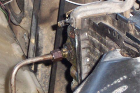 1980 Ford Bronco - Close-up of a copper hard line threaded into a brass fitting on a bracket at the front of an engine bay, with the radiator core and a corro…