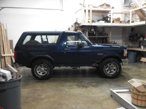 1995 Ford Bronco - A dark blue Ford Bronco SUV is parked inside a garage, showing its side profile.