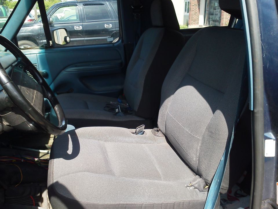 Interior of a truck with cloth seats and a steering wheel. Another SUV is visible through the window
