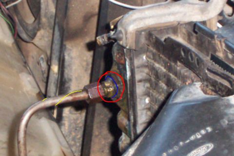 1980 Ford Bronco - Close-up under the hood of a brass fitting and hex nut on a metal line, circled in hand-drawn red with blue and yellow marker lines tracing…