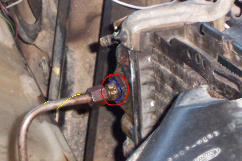 Brass line fitting circled in red marker on rusty bracket near radiator support