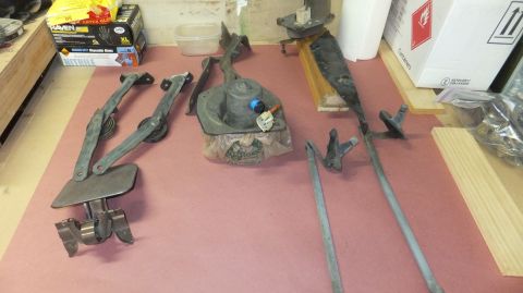 1983 Ford Bronco - Various disassembled windshield wiper components are laid out on a pink surface, with boxes and other items in the background.