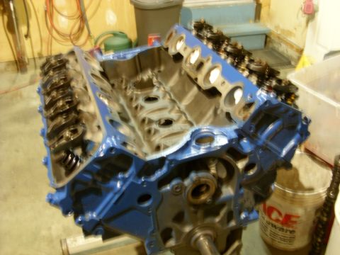1967 Ford F-250 - A blue V8 engine block is shown, partially assembled with valve train components, in a workshop setting.