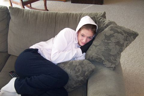 1980 Ford Bronco - Indoor snapshot of a person in a white hooded sweatshirt and black sweatpants curled up on a beige couch with patterned throw pillows, a TV…