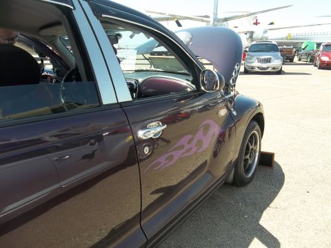 2005 Chrysler PT Cruiser - A custom purple Chrysler PT Cruiser with flame decals is parked outside with its hood up.