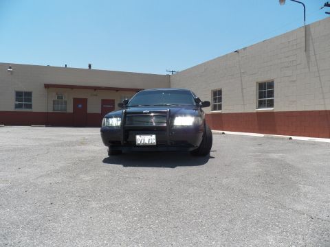 2003 Ford Crown Victoria - Head-on shot of a black Crown Victoria with brush guard and headlights illuminated.