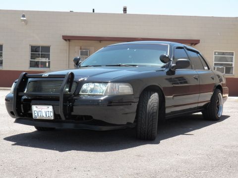 2003 Ford Crown Victoria - Tight front-quarter of a black Crown Victoria; brush guard and EVIL VIC plate visible.