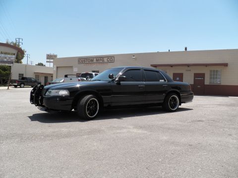 2003 Ford Crown Victoria - Black Crown Victoria with brush guard photographed beside a Custom Mfg Co storefront.
