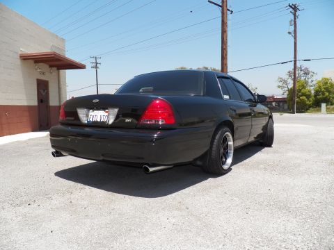 2003 Ford Crown Victoria - Lowered black Crown Victoria from rear right; SVT badge and EVIL VIC plate near a concrete building.