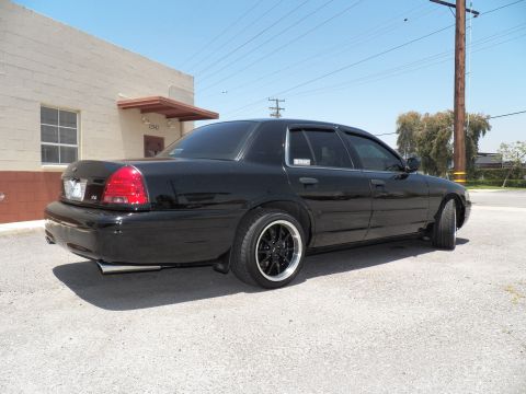2003 Ford Crown Victoria - Lowered black Crown Victoria sedan shown from the right rear with whitewall-trimmed black wheels.